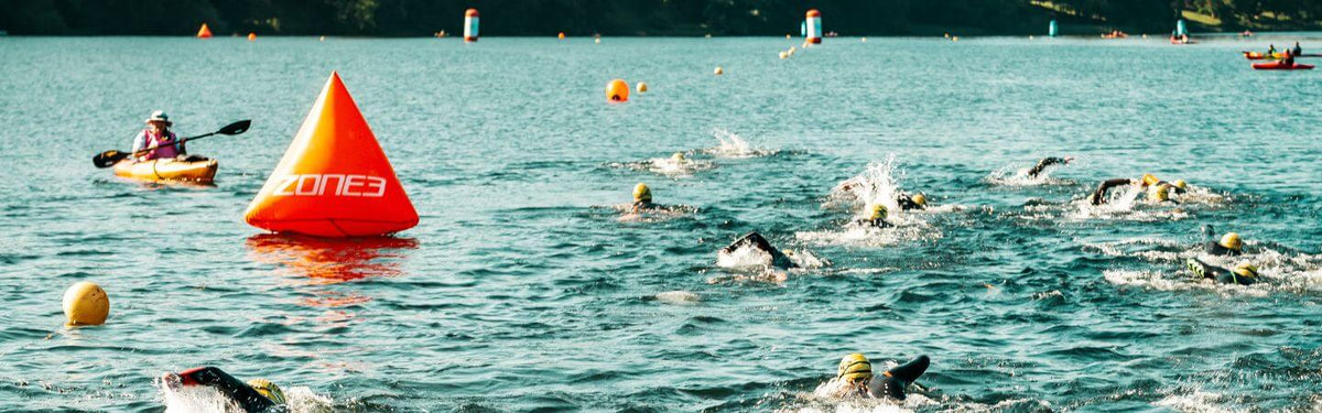 un groupe de personnes nage lors d'une épreuve en eau libre, avec une bouée de virage dans l'eau