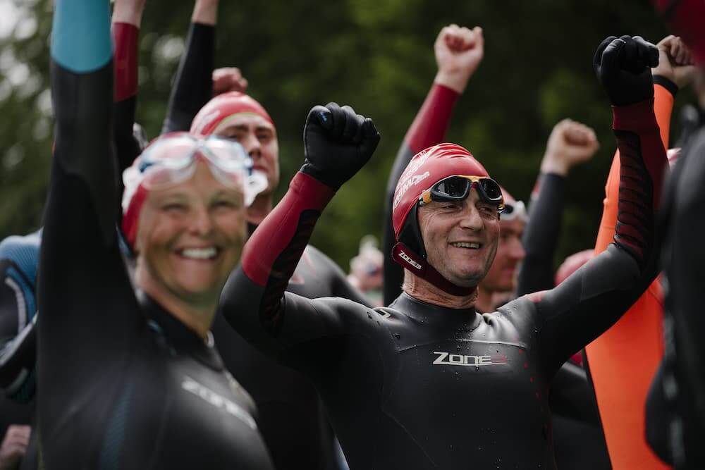 Nageurs en combinaisons néoprène noires et bonnets de bain rouges levant les bras pour célébrer lors de la Great North Swim.