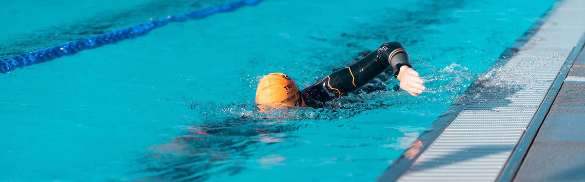 Nageur en bonnet orange enchaînant les longueurs dans une piscine turquoise avec une ligne d'eau