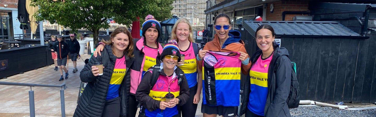 Membres du club Swansea Vale Tri en maillots aux couleurs vives posant ensemble au bord de l'eau.