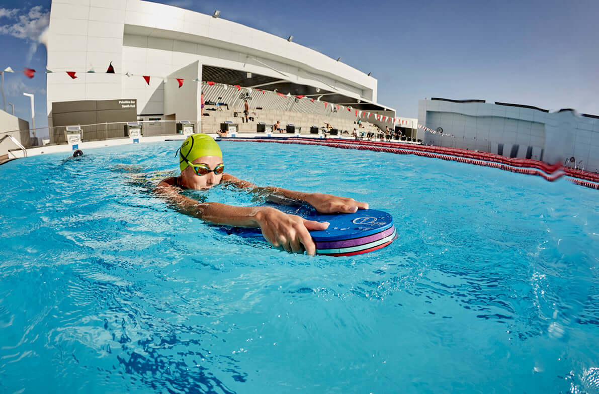 Nageur en bonnet vert citron et lunettes de natation tenant une bouée circulaire bleue dans une piscine extérieure