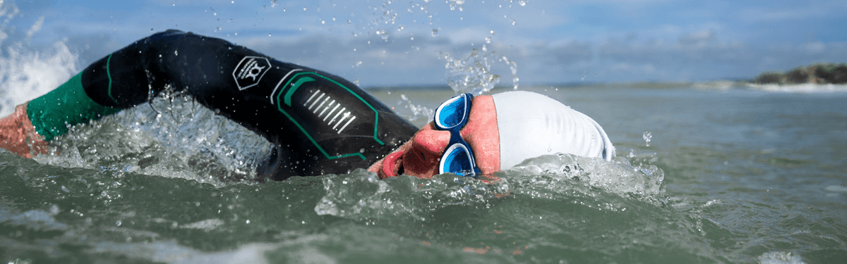 un homme nage en eau libre en respirant d'un côté, lunettes de natation face à l'objectif