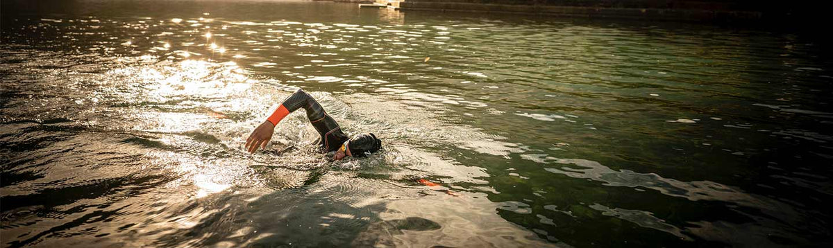 Nageur en eau libre en combinaison néoprène glissant dans une eau baignée de soleil.