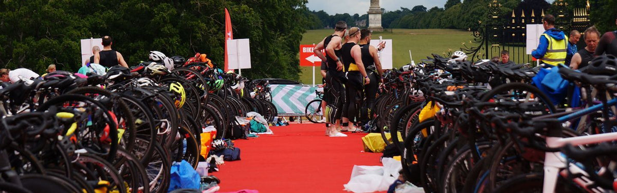 une aire de transition de triathlon avec tous les vélos rangés sur les racks et beaucoup de matériel de chaque côté, le tout sur un tapis rouge