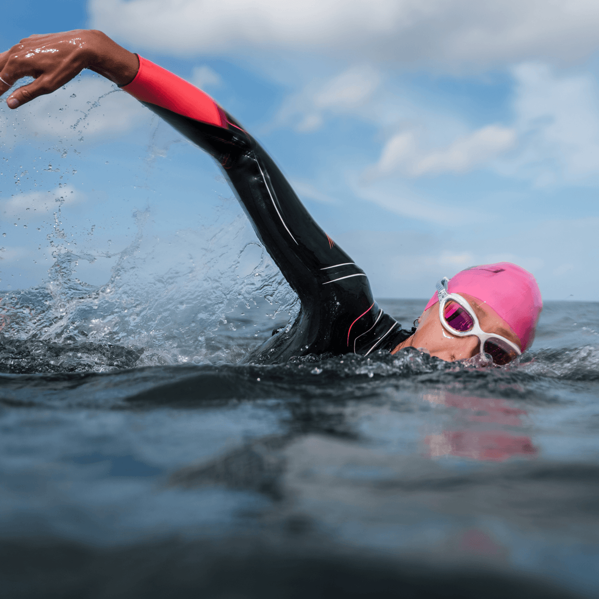 Swimmer's arm in a black and pink wetsuit sleeve splashes water during a swim.