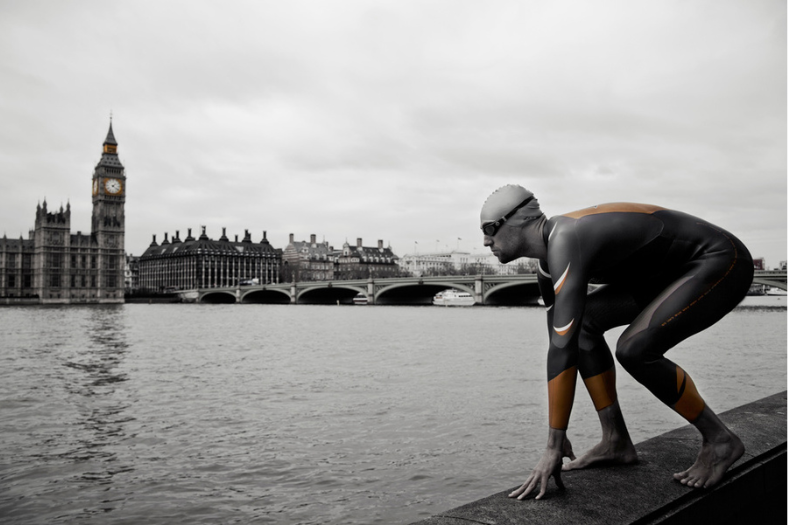 Image en noir et blanc avec le Parlement de Londres en arrière-plan : un homme en combinaison néoprène ZONE3 prend la pose sur le muret de la Tamise.