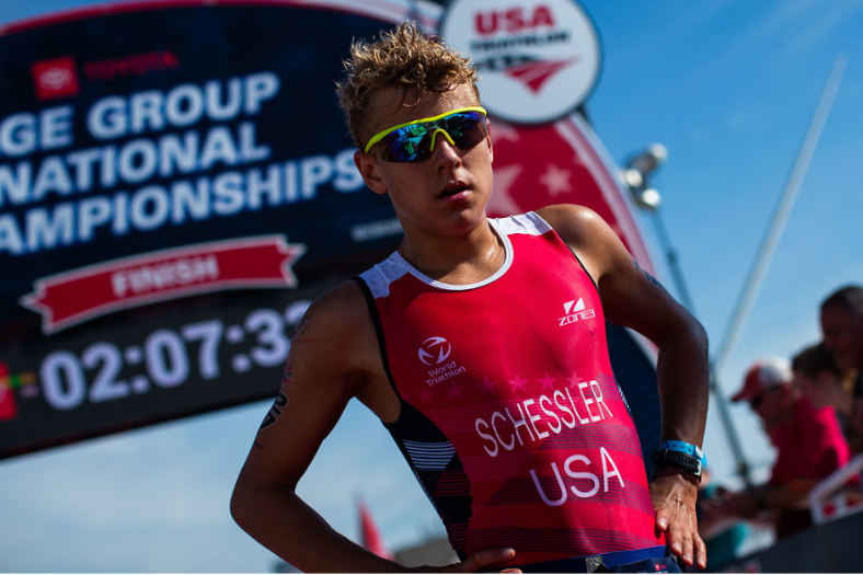 Athlète américain sur la ligne d'arrivée d'un triathlon. Il porte une trifonction rouge floquée du nom Schessler et des lunettes de soleil de course jaunes polarisées.