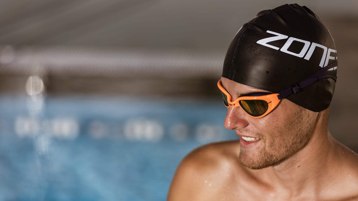 Man wearing a Zone3 black swim cap and attack Navy/Neon Orange
 goggles