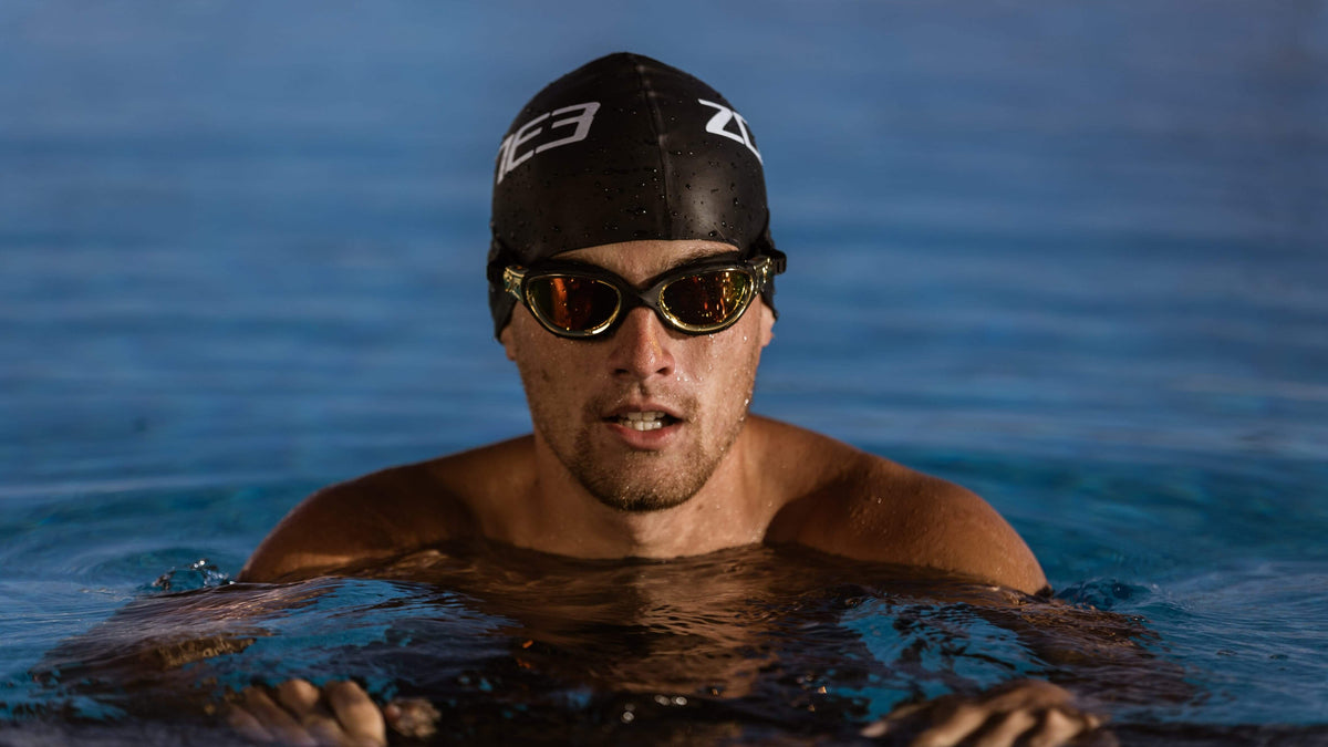 athlete wearing a black Zone3 swim cap and the black metallic gold goggles in the water