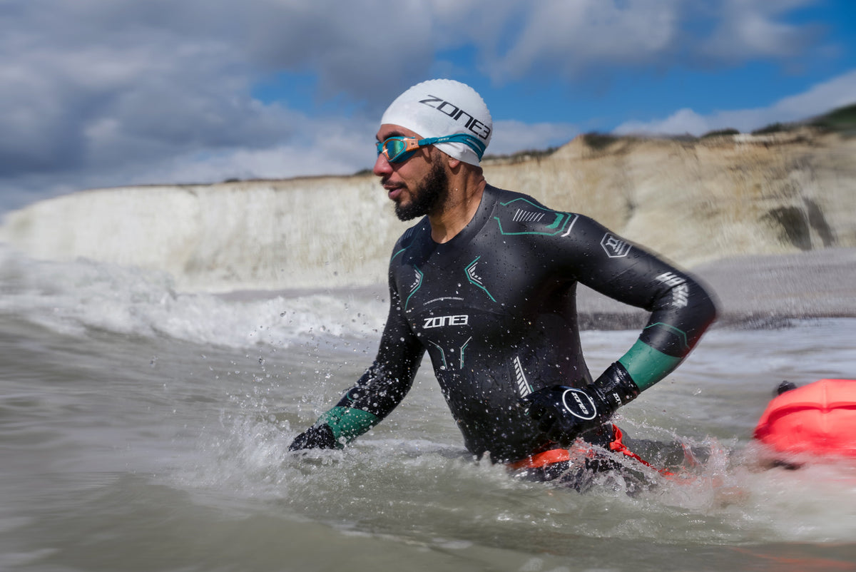 Person in a wetsuit and swim cap emerging from water with Zone3 branding.