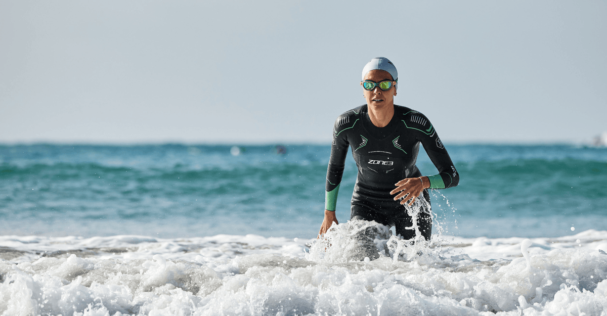 Person in a wetsuit and swim cap emerging from the ocean waves.